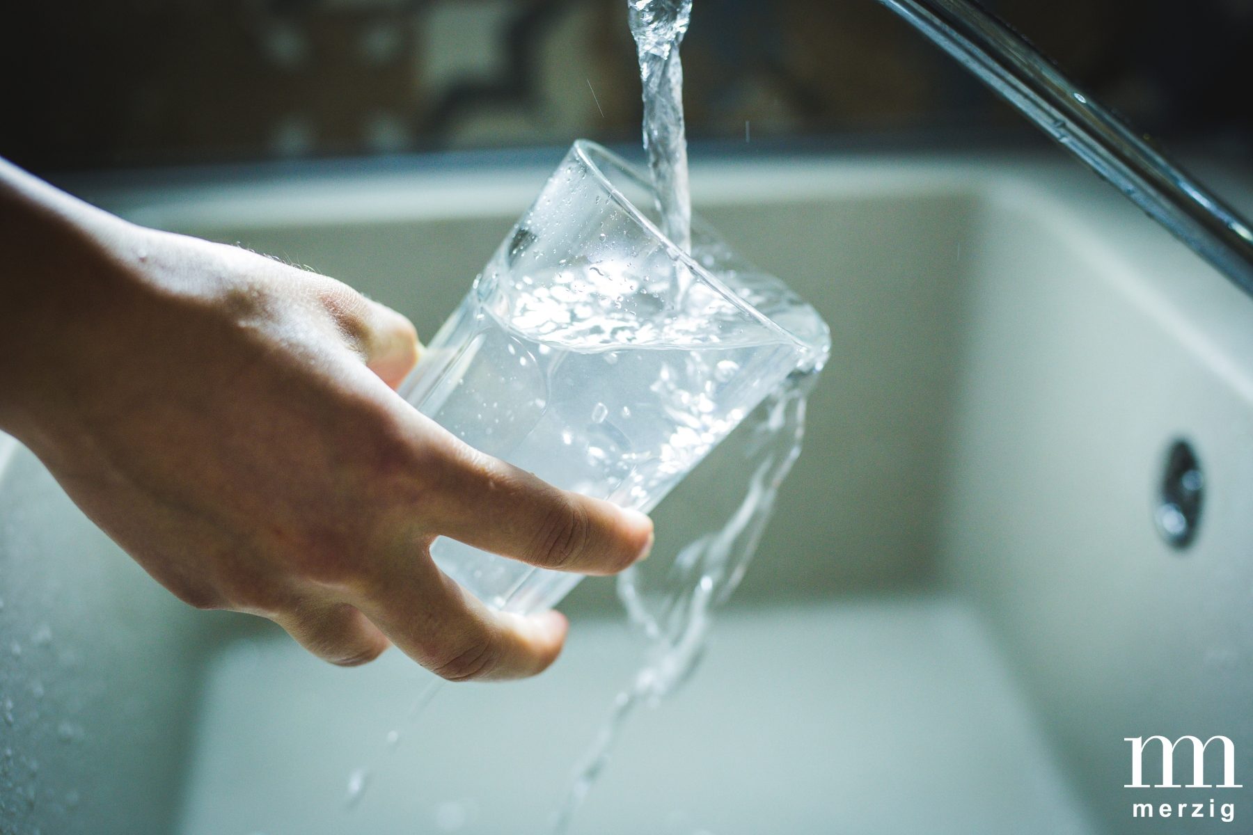 Hand hält ein Wasserglas unter fließendes Wasser