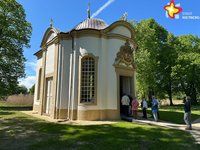 Einige Menschen stehen vor der Tür einer kleinen, weißen Kapelle. Der Himmel strahlt blau.