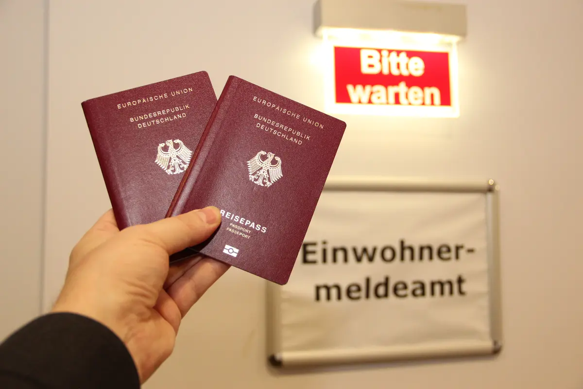 Eine Person hält zwei Pässe vor dem Eingang des Einwohnermeldeamtes.