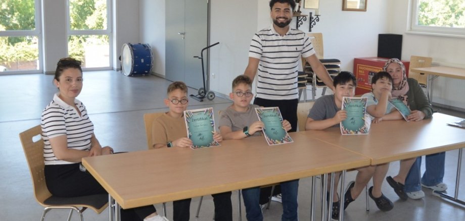 Kinder und eine Frau an einen Tisch sitzend ein Mann stehend