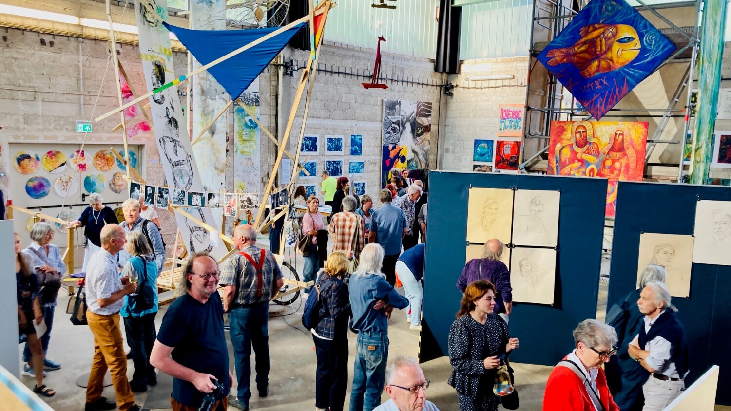 In einer Halle sind Personen, die sich aufgehangene und ausgestellte Kunstwerke anschauen.