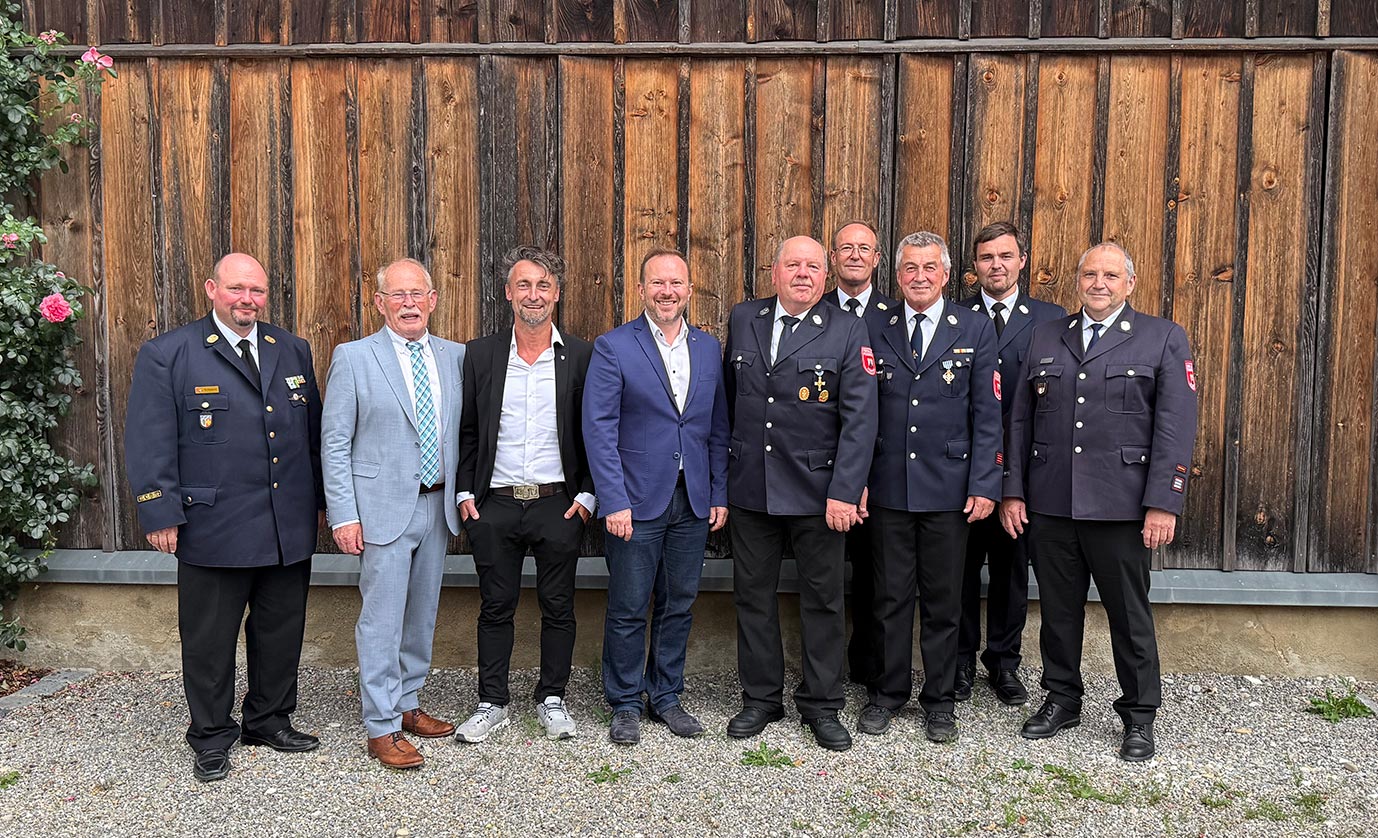 Anlässlich der Ehrung zweier Mitglieder der Feuerwehr Mering stehen zwei stellv. Landräte, Bürgermeister Florian A. Mayer und mehrere Feuerwehrkameraden in einer Reihe für ein Gruppenfoto. | © Georg Egenhofer