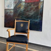 Zu sehen ist ein Ratsstuhls (Vorderansicht) mit Brühler Stadtwappen vor einem Gemälde