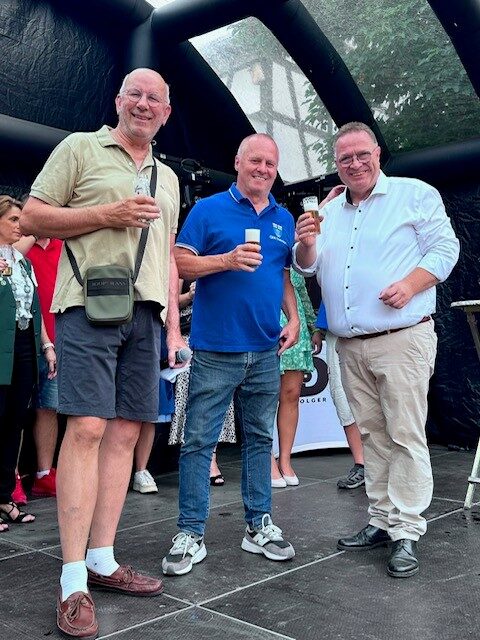 Drei Männer stehen mit einem Bier in der Hand auf einer Bühne und sind dem Fotografen zugewandt