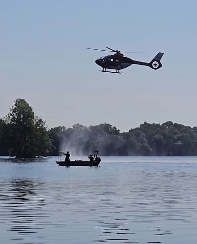 Bild: Ein Rettungshubschrauber im Tiefflug über einem See, auf dem ein Rettungsboot der Feuerwehr mit Besatzung schwimmt.