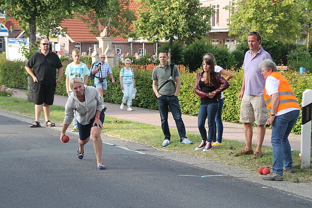 Eine Frau schmeißt eine Boßelkugel. Weitere Personen stehen am Straßenrand.
