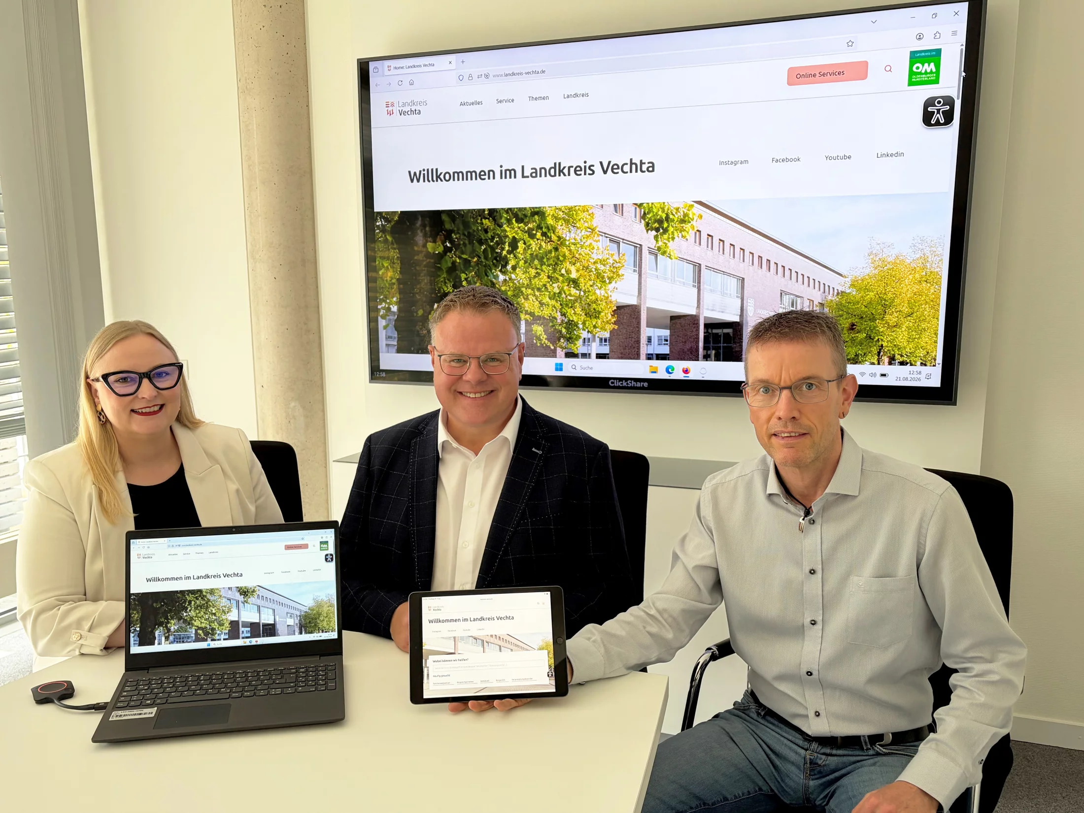Drei Personen sitzen an einem Tisch und präsentieren einen Laptop und ein Tablet.