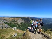 Drei Jugendliche stehen auf einem Berg und schauen auf die Berglandschaft und den blauen Himmel.