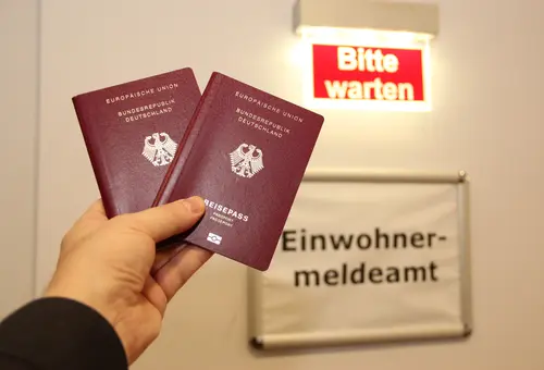 Eine Person hält zwei Pässe vor dem Eingang des Einwohnermeldeamtes.