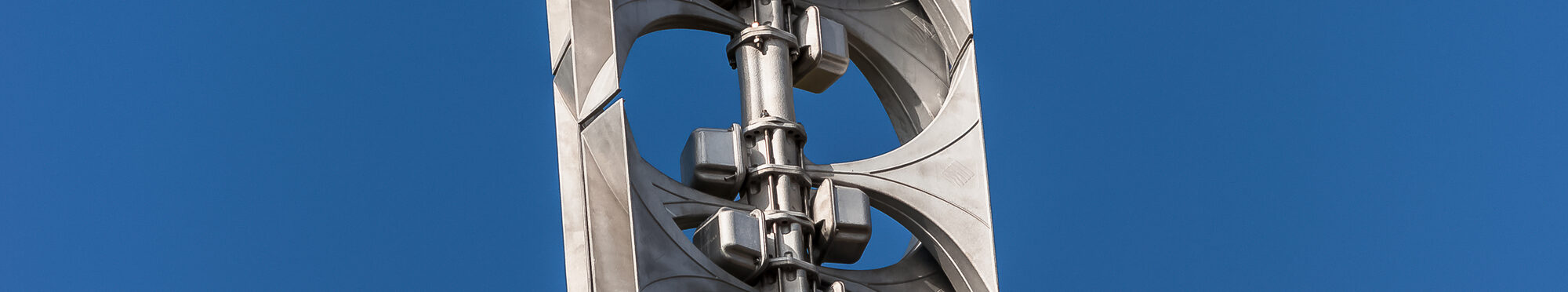 Nahaufnahme einer Sirenenanlage mit mehreren grauen Lautsprechern auf einem hohen Metallmast vor blauem, wolkenlosem Himmel.