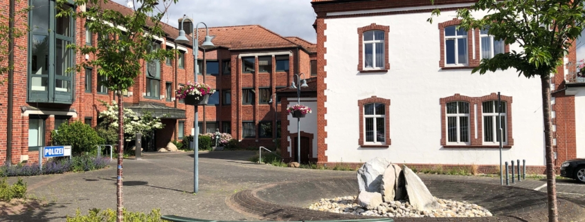 Rathaus mit Ziegel- und Putzfassaden, Sitzbank, Pflanzen und Steine im Vordergrund