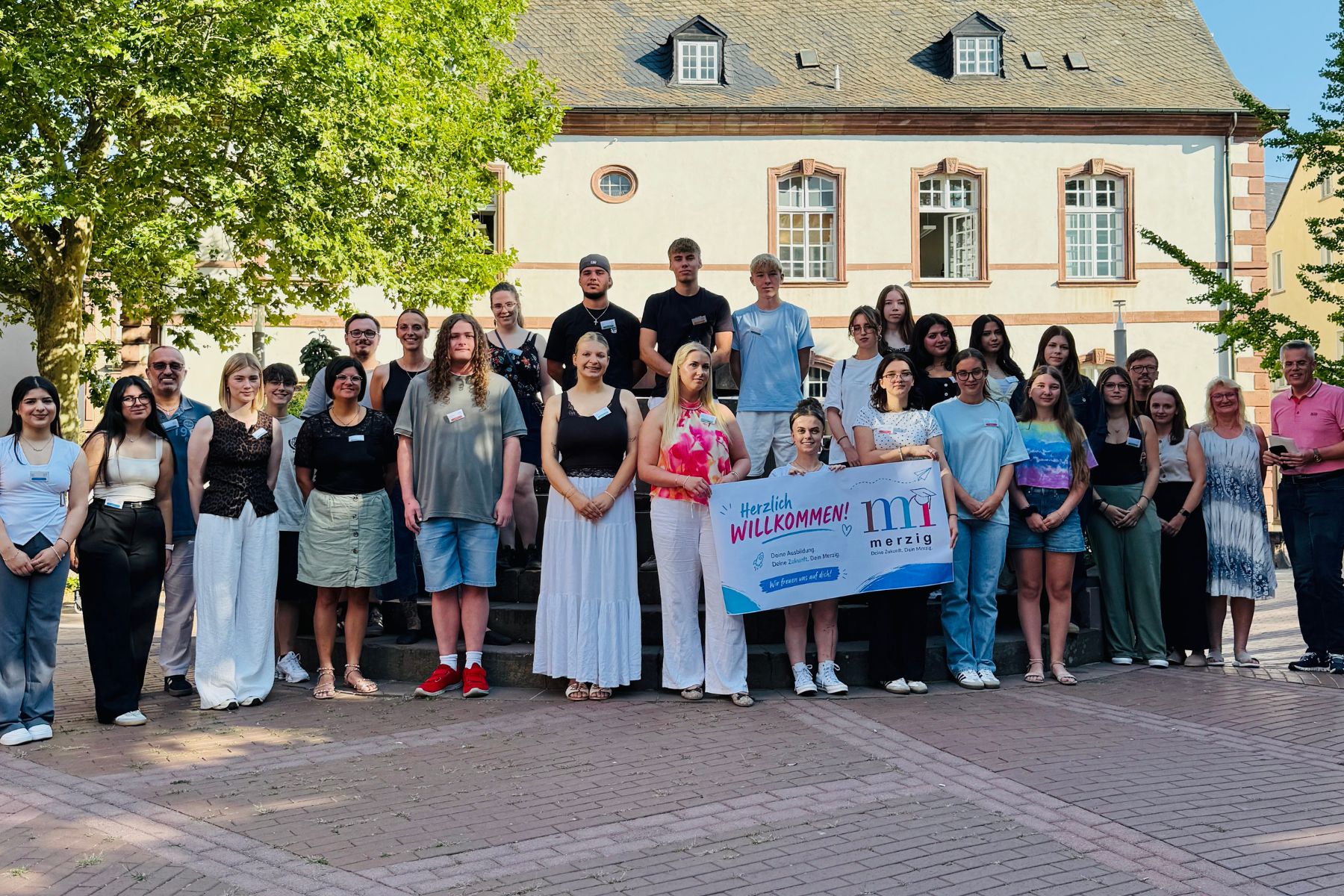 Gruppenfoto des Verwaltungsnachwuchses im Rathaus-Innenhof, drei Mädchen halten ein Willkommensschild