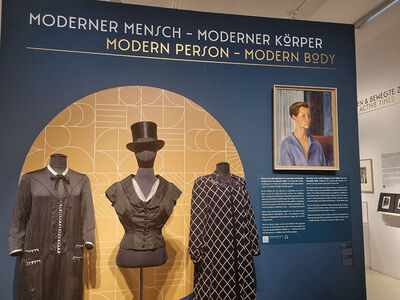 Stellwamd der Ausstellung mit Modebeispielen und einem Frauenporträt.