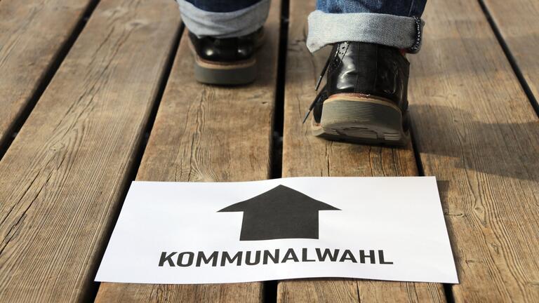 Das Bild zeigt einen Zettel, auf dem Boden liegend. auf ihm steht Kommunalwahl. dahinter sind Schuhe zu sehen. steht