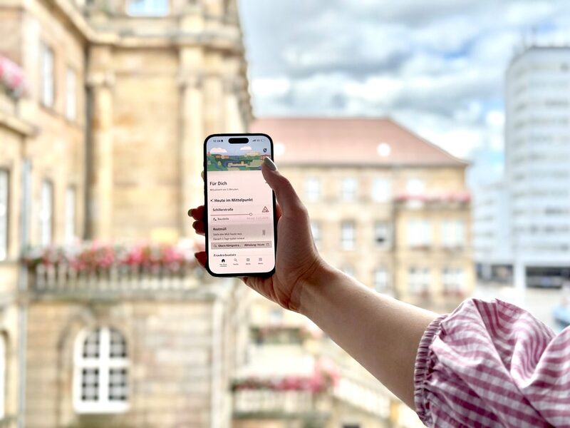 Im Bild hält eine Hand ein Handy hoch, die Kassel-App ist geöffnet