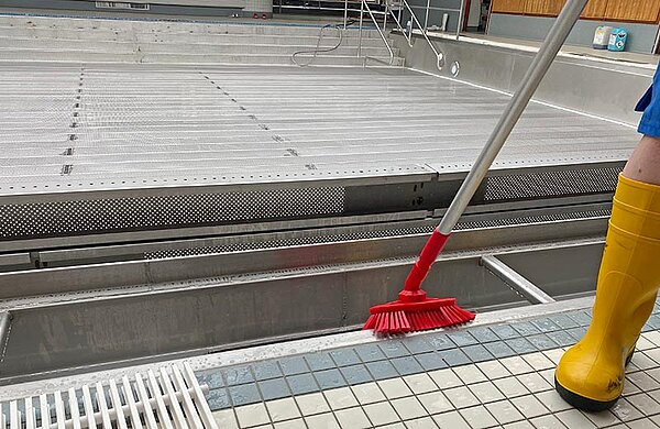 Der Beckenrand eines Schwimmbeckens wird mit einer Bürste gereinigt.