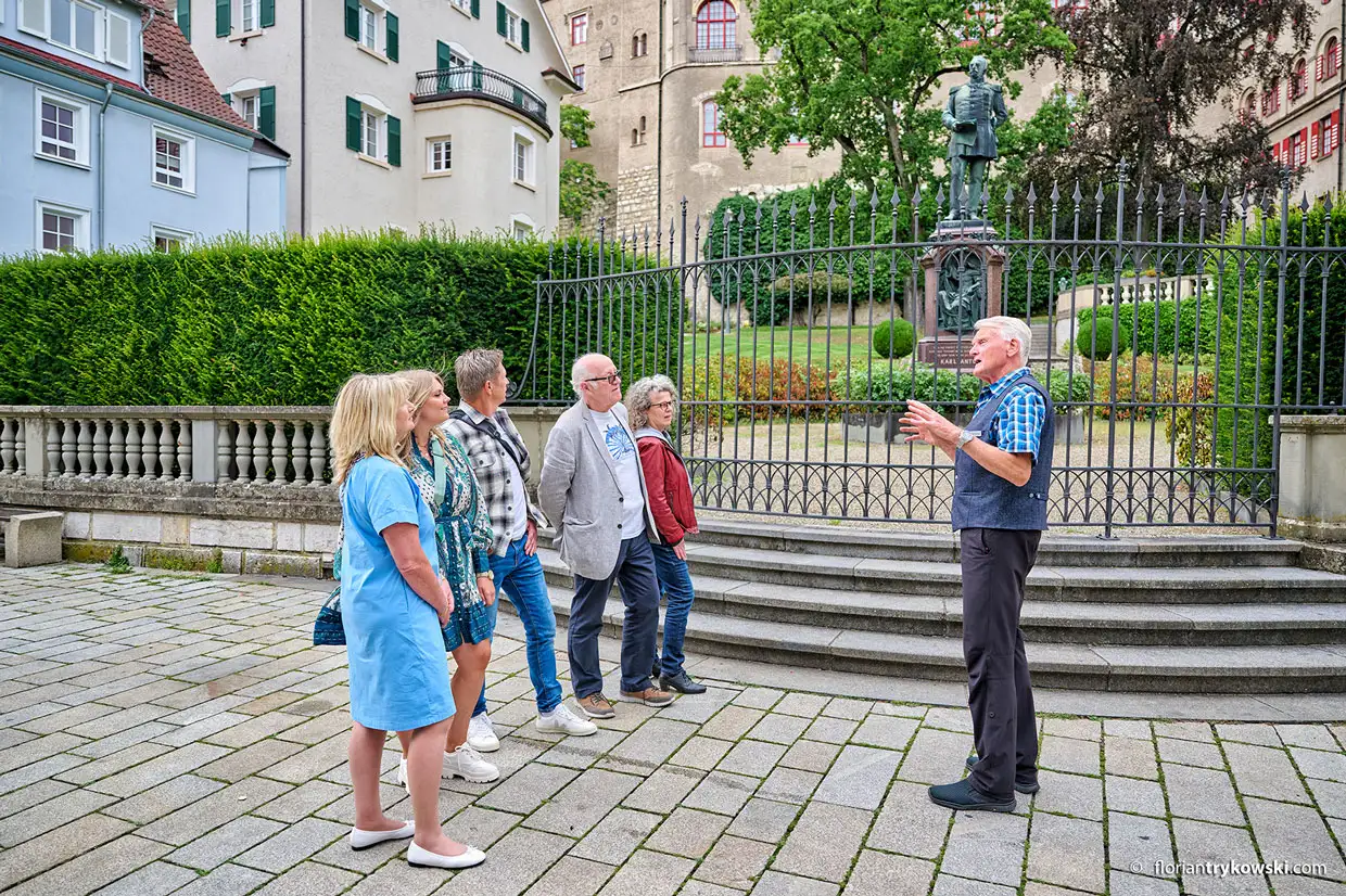 Ein Stadtführer und eine kleine Gruppe von fünf Personen stehen auf dem Karl-Anton-Platz.