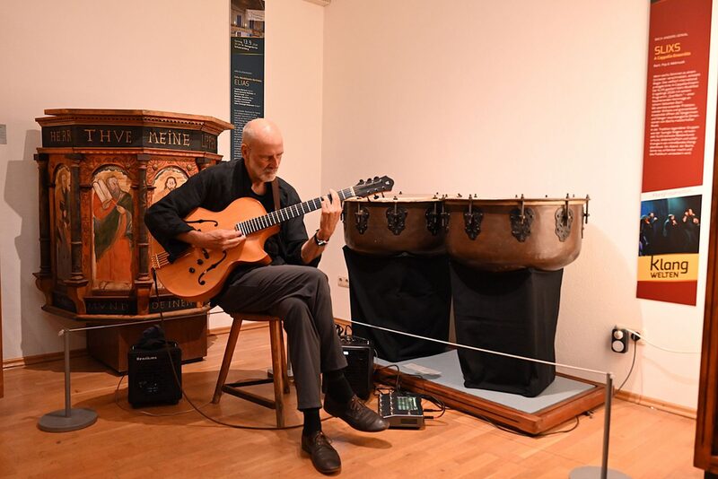 Musiker sitzend mit Gitarre im Ausstellungsraum