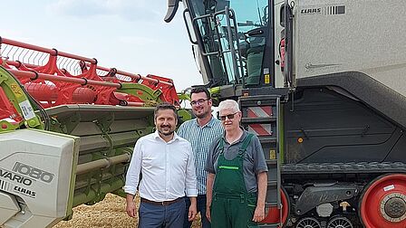 Drei Männer stehen vor einem großen Mähdrescher auf einem Getreidefeld