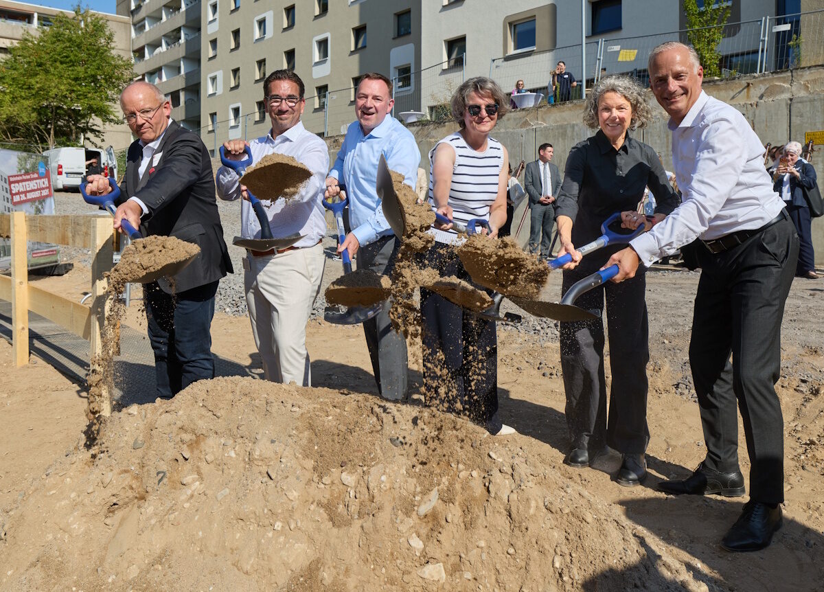Sechs Personen schaufeln Erde für für einen symbolischen Spatenstich aus einer Grube.