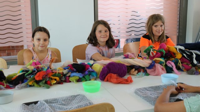 Kinder sitzen auf dem Stuhl vor dem Tisch mit bunter Schafwolle