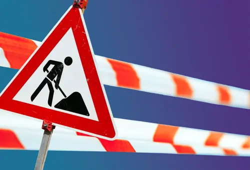 Ein Schild weist auf Bauarbeiten hin, Flatterband auf Absperrungen.