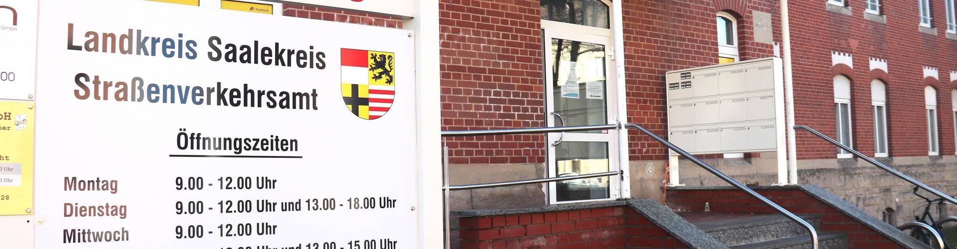 Ein rotes Backsteingebäude, man sieht den Eingang mit Treppe, davor das Schild mit Öffnunsgzeiten