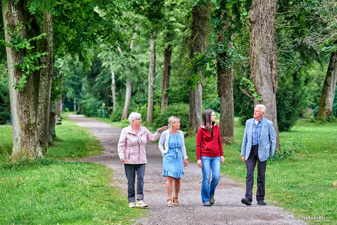 Vier Personen spazieren durch einen Park mit Bäumen.