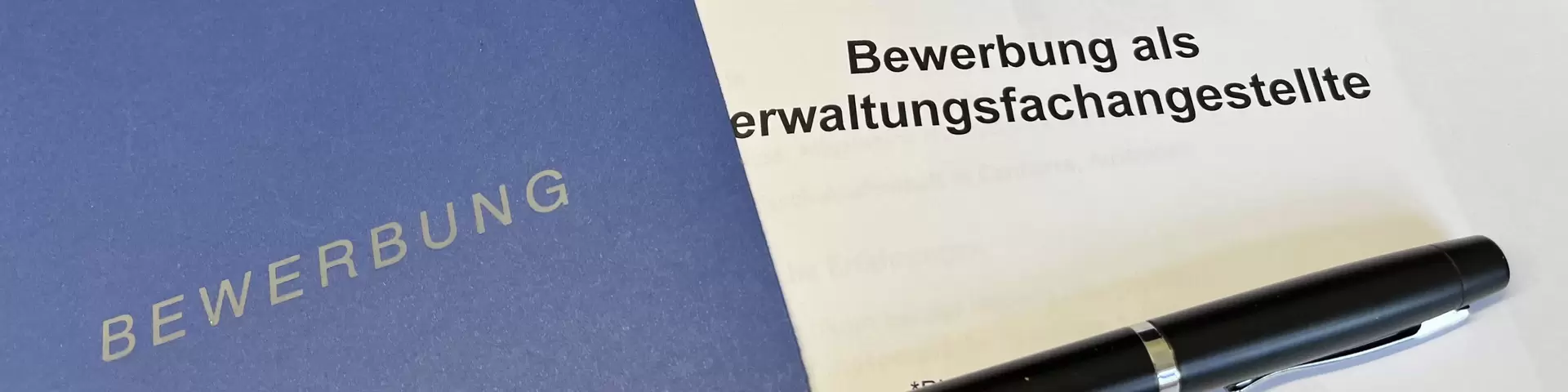 Bewerbungsmappe mit Kugelschreiber liegt neben einer Computertastatur