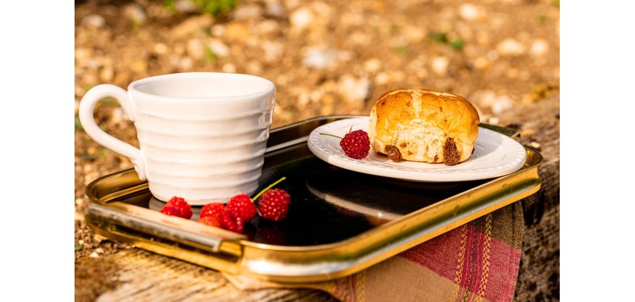 Auf dem Bild ist eine Tasse Kaffee und Gebäck mit ein paar Himbeeren zu sehen
