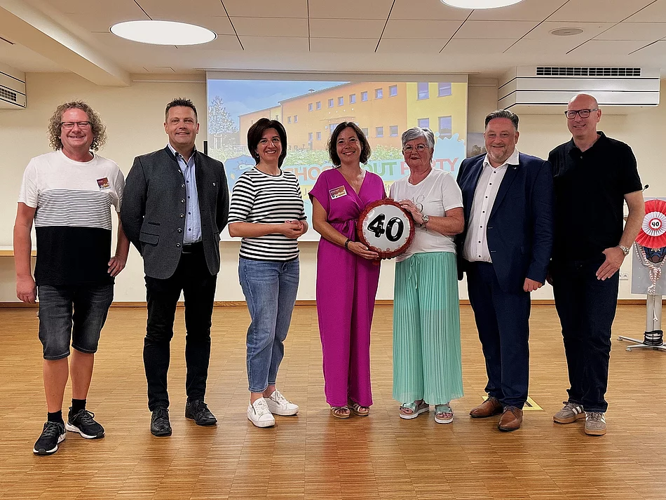 Sieben Personen stehen bei einer Feierstunde im Mehrgenerationenhaus nebeneinander, in der Mitte wird ein symbolisches Jubiläumszeichen mit der Zahl 40 präsentiert.