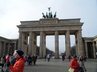 Das Brandenburger Tor mit seinen hohen Säulen und der Figur der Wagenlenkerin und ihren Pferden oben auf dem Tor. Davor stehen Besucherinnen und Besucher.